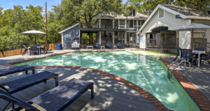 Pool with lounge chairs. Behind the pool is the office and many, many trees.